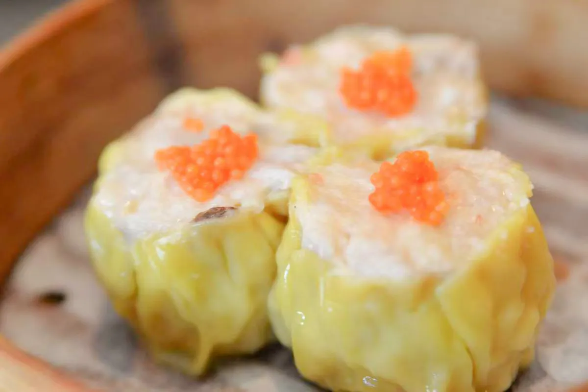 Three siu mai dumplings topped with orange fish roe inside a bamboo steamer at One More Bite Dumpling, a Chinese Restaurant in Palm Desert