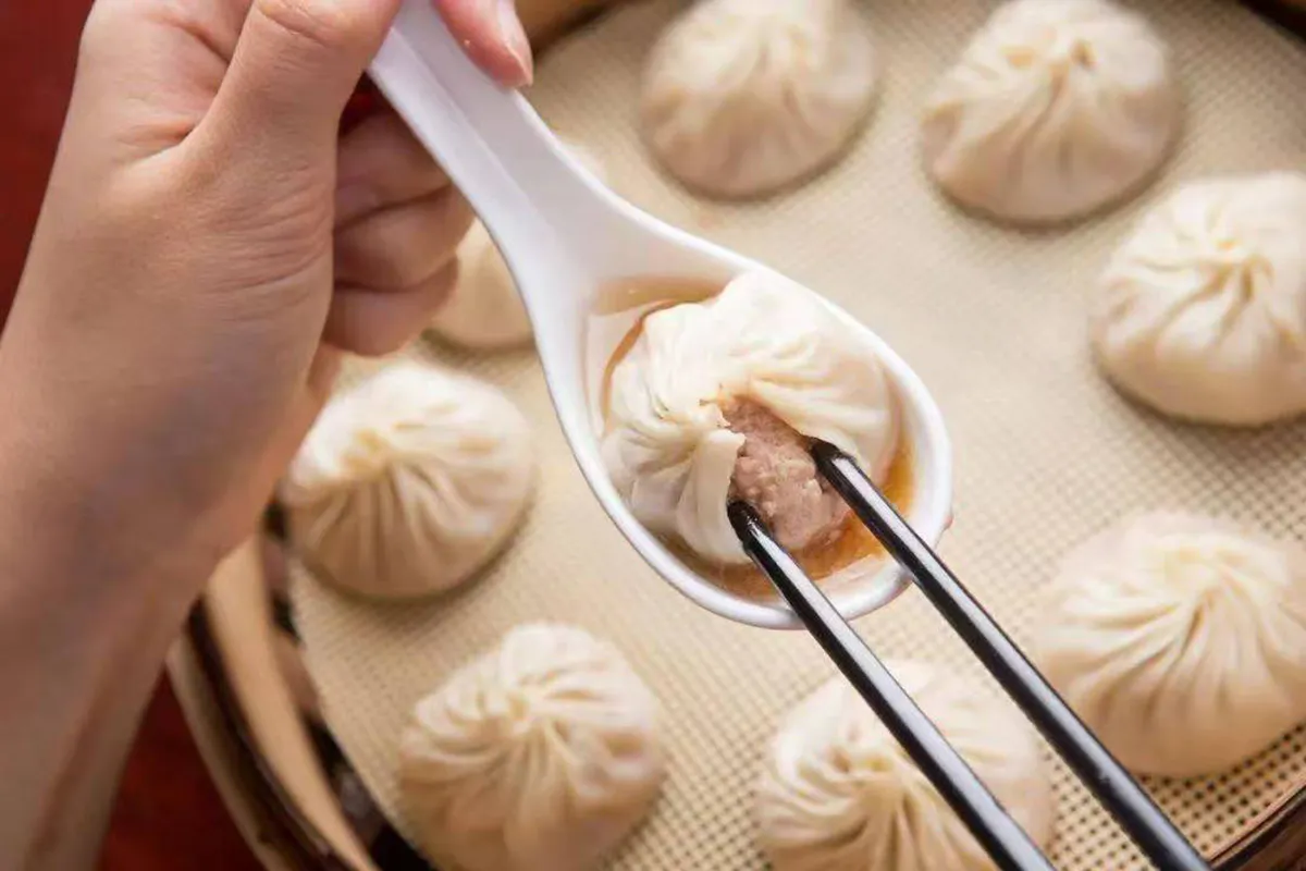 Soup dumpling held on a white spoon with chopsticks above bamboo steamer baskets at One More Bite Dumpling, a Chinese Restaurant in Palm Desert
