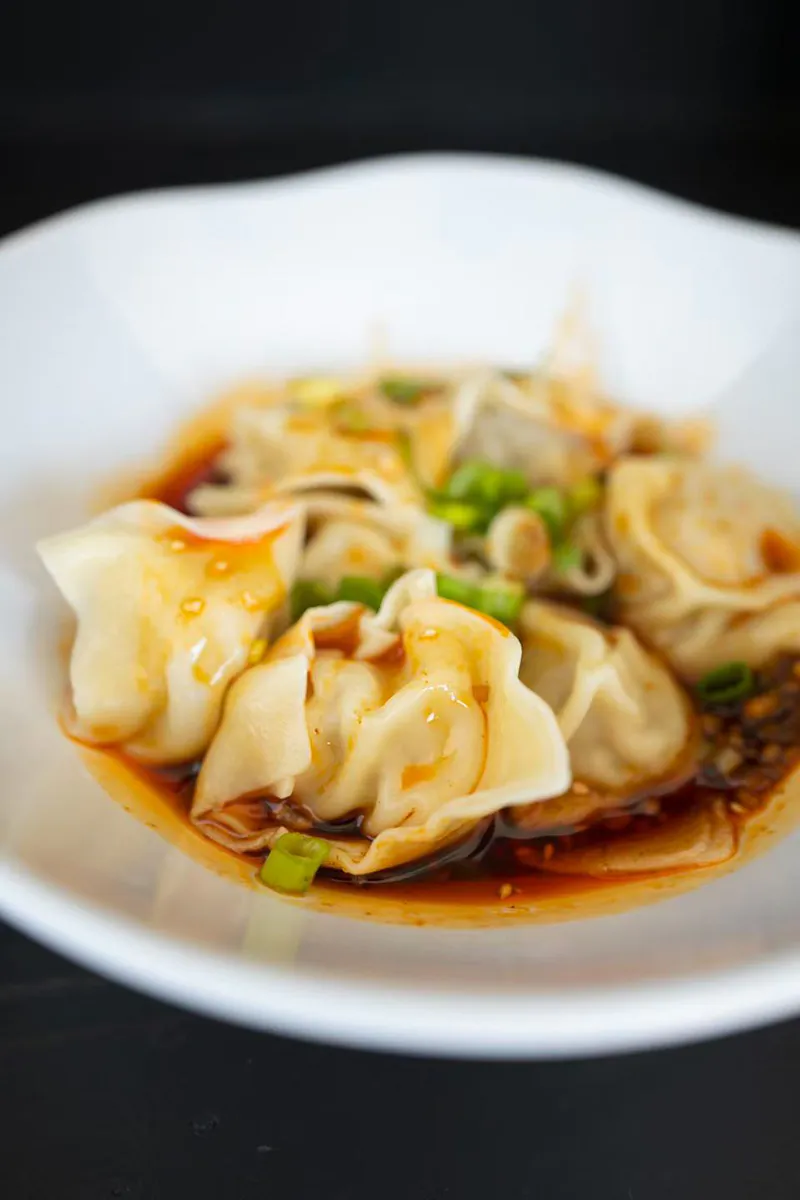 Spicy boiled dumplings served in red chili sauce topped with chopped green onions at One More Bite Dumpling, a Chinese Restaurant in Palm Desert