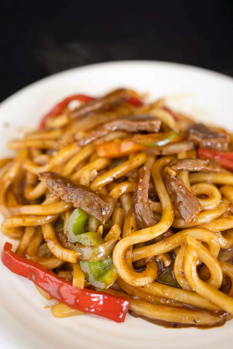 Beef udon stir fry mixed with bell pepper strips and glossy dark sauce at One More Bite Dumpling, a Chinese Restaurant in Palm Desert