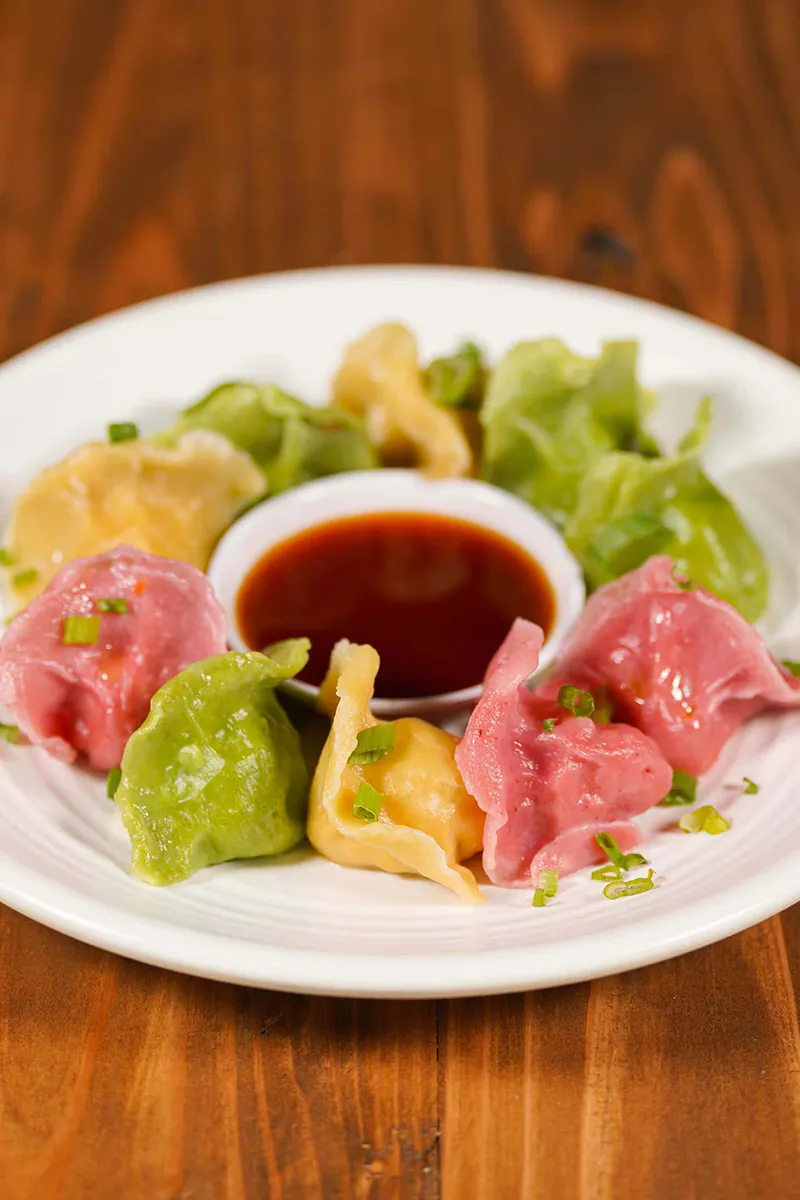 Assorted colorful vegetable dumplings arranged on plate with side soy dipping sauce at One More Bite Dumpling, a Chinese Restaurant in Palm Desert