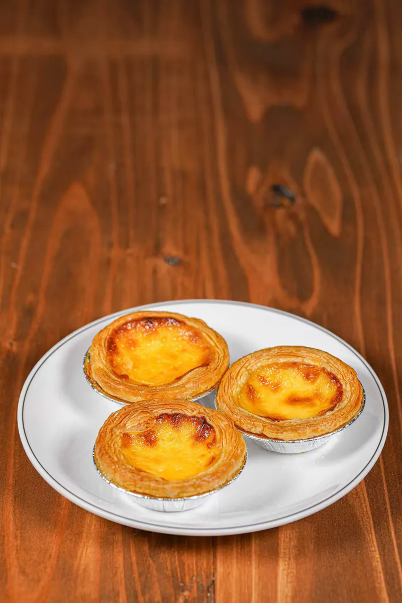 Three baked egg tarts with flaky pastry crust on simple white plate at One More Bite Dumpling, a Chinese Restaurant in Palm Desert