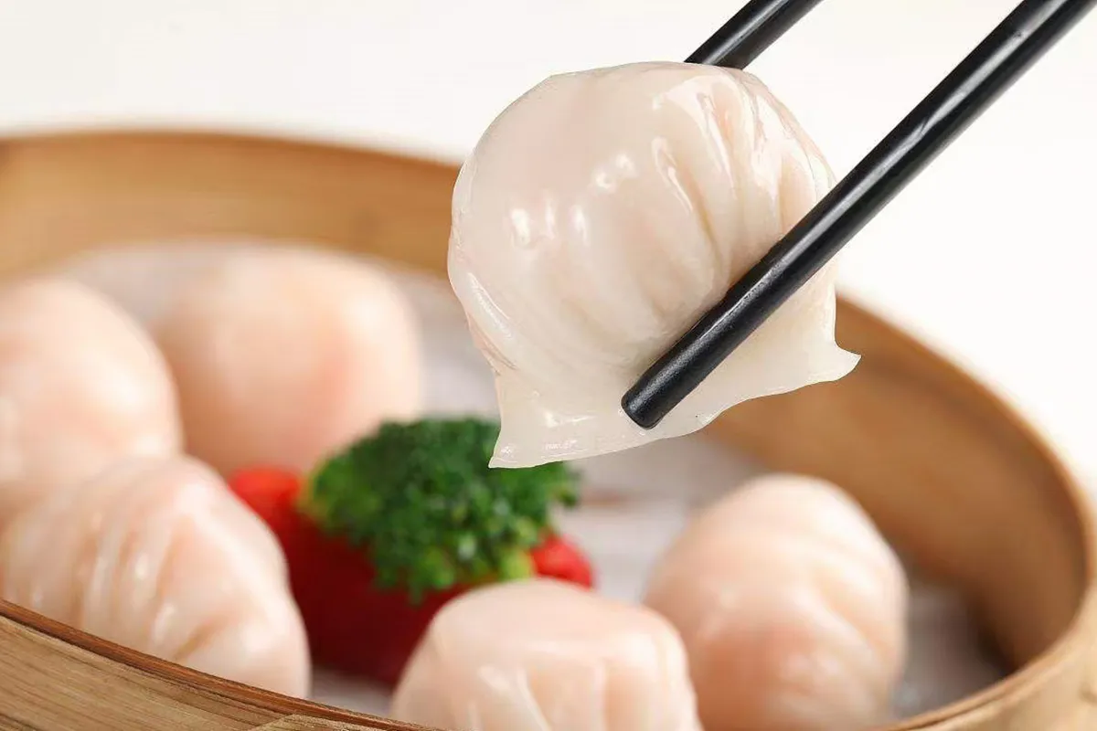 Shrimp har gow dumpling held by chopsticks above bamboo steamer basket at One More Bite Dumpling, a Chinese Restaurant in Palm Desert
